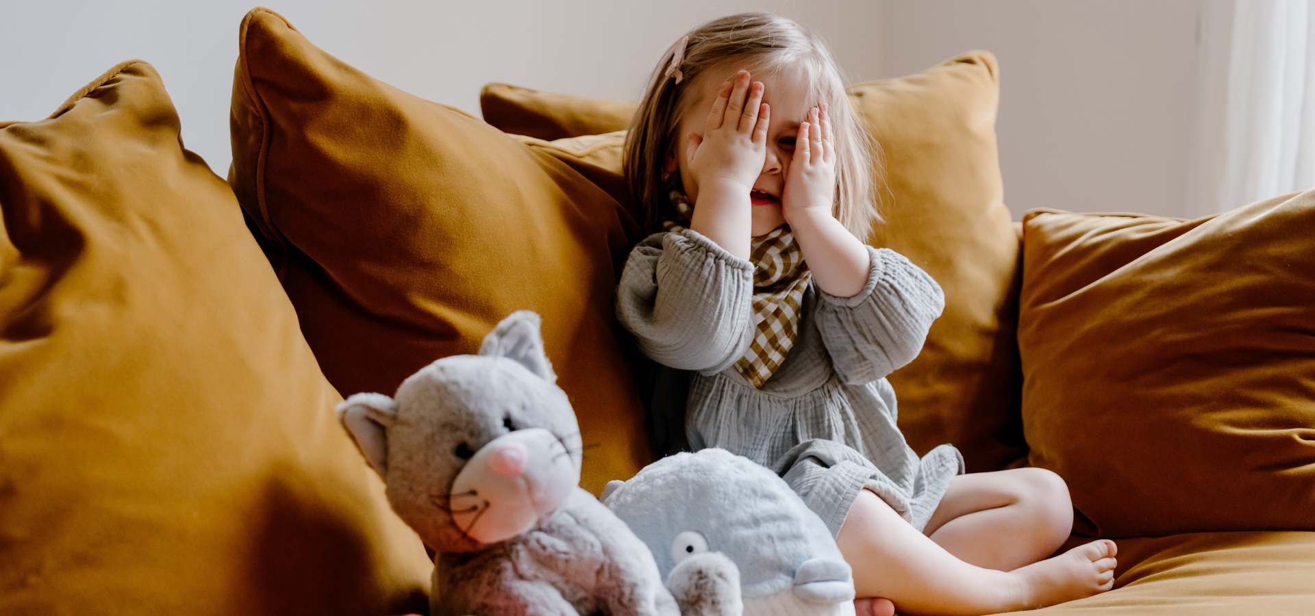 Petite fille dans un canapé avec des bouillottes peluches se cachant les yeux. 