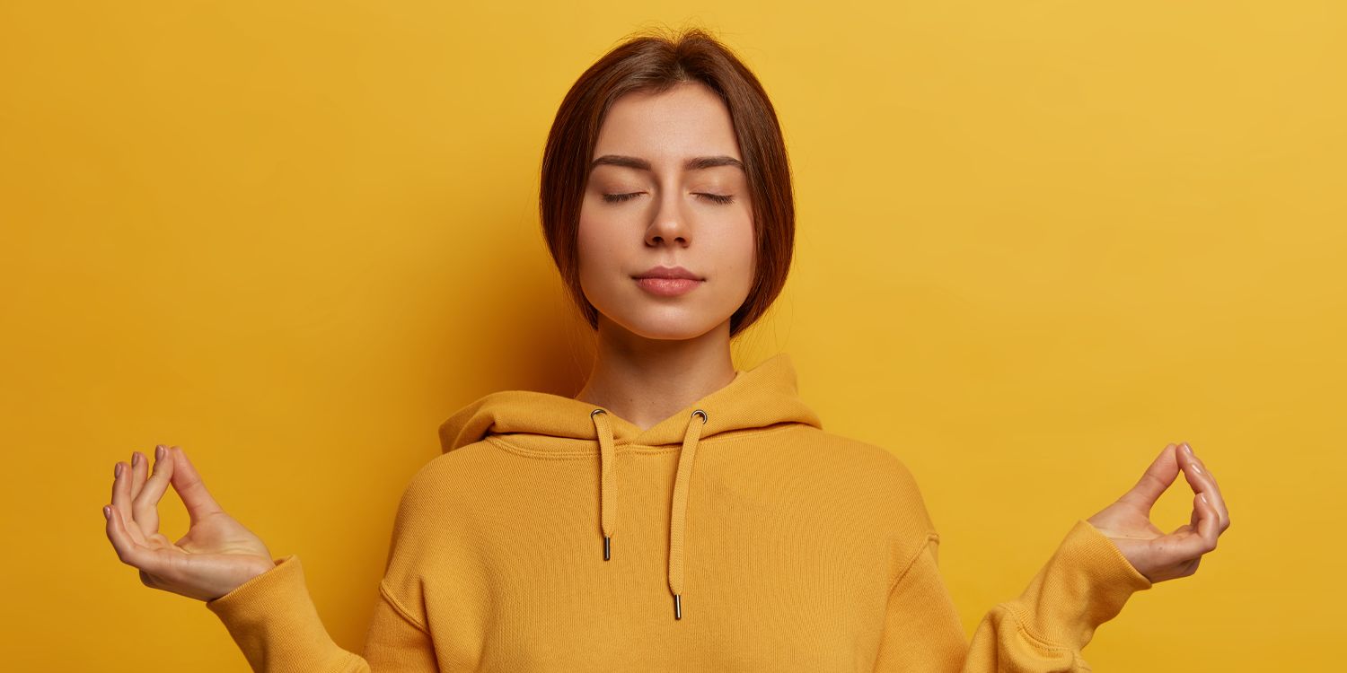 Femme sur fond jaune, position de détente, les yeux fermés, faisant avec ses mains des signes de méditation, signe zen