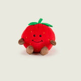 Bouillotte peluche en forme de fraise, rouge avec sur le haut deux feuille et une tige verte. Elle a un visage avec un sourire, des bras et des jambes marron