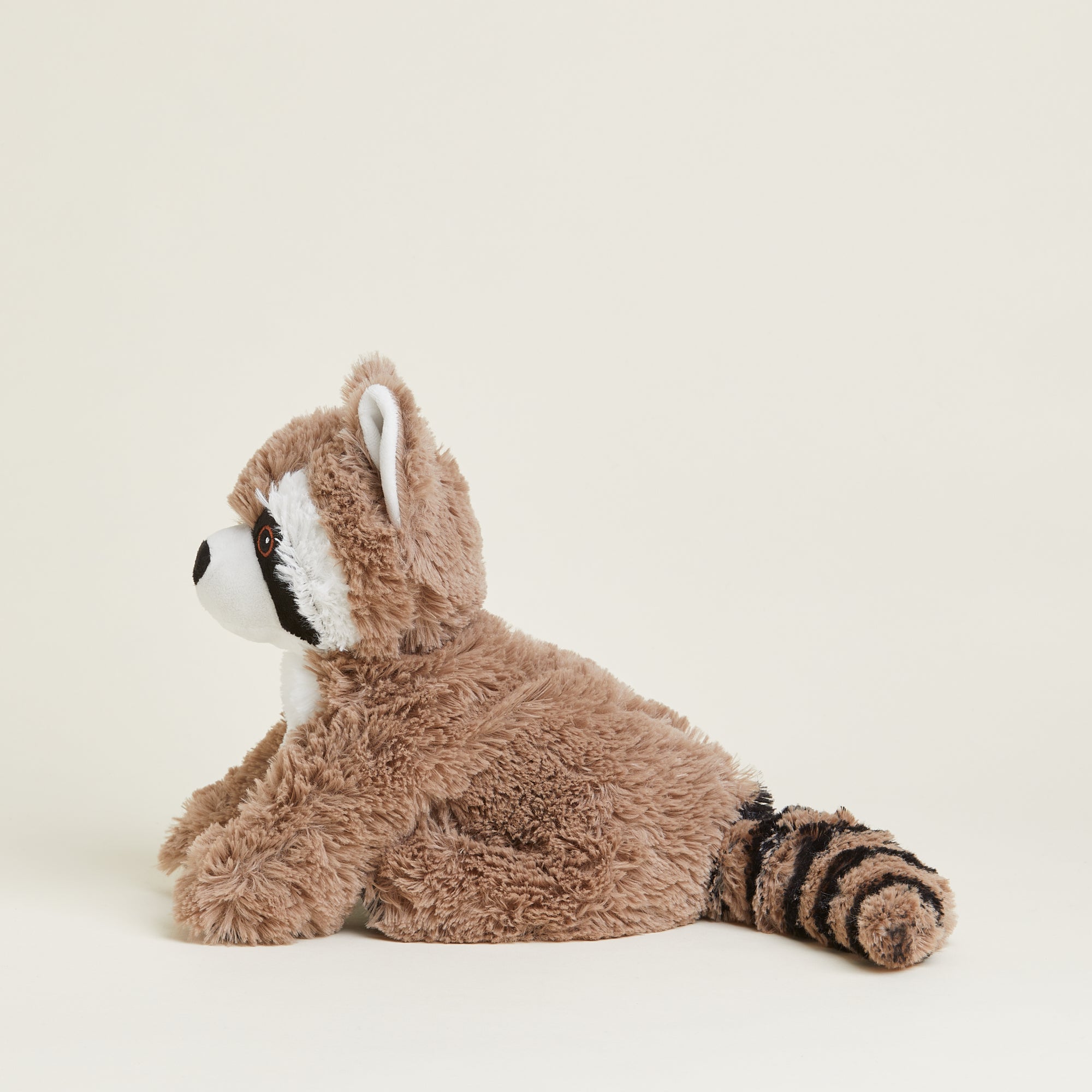 Bouillotte peluche en forme de raton laveur. Pelage marron et noir et tête blanche. Position assise. Queue rayée noire et marron. Positionné de profil. 