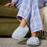 pied d'une personne en pyjama, installée sur son canapé, portant a ses pieds les chaussons bouillottes gris de la marque Warmies 