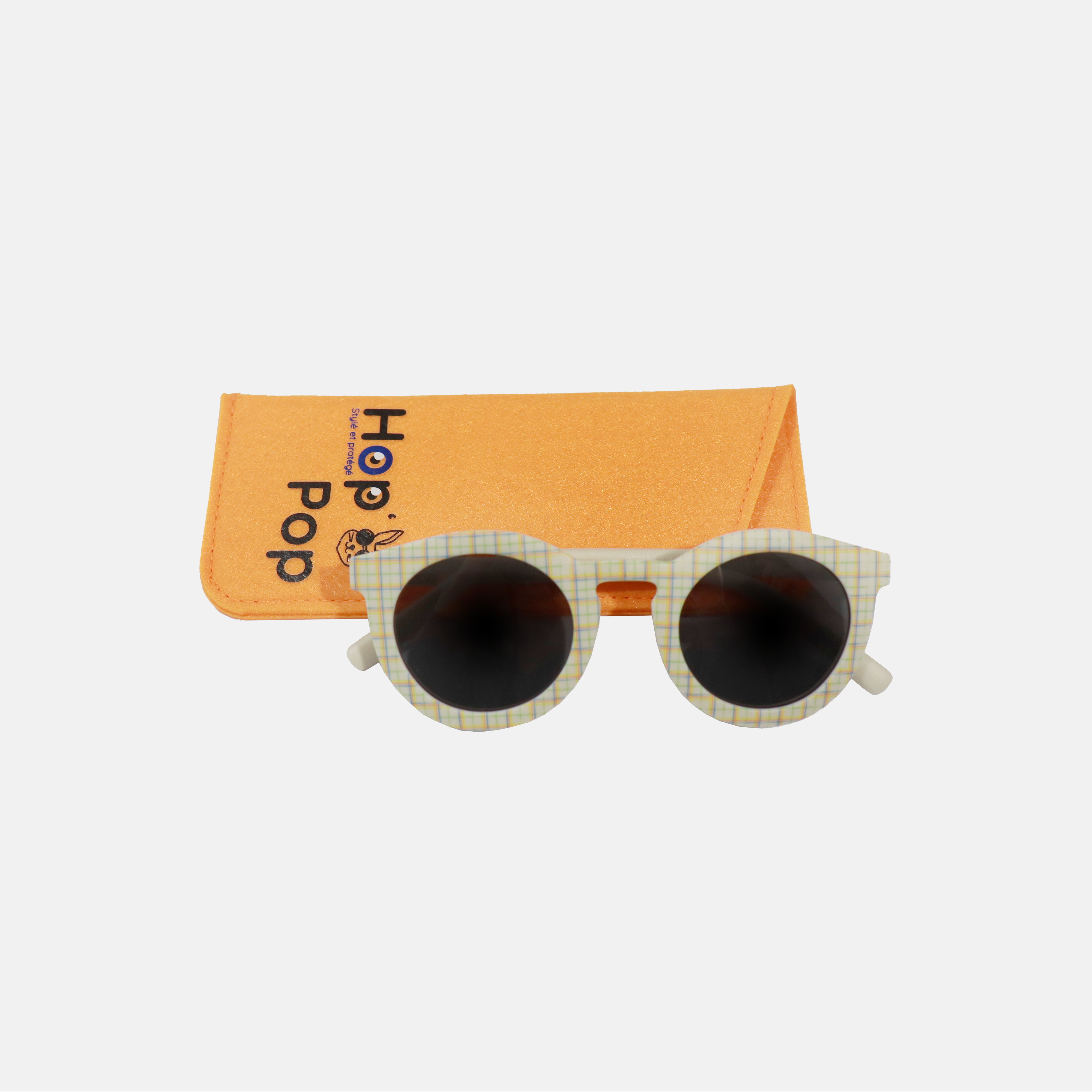 Lunettes de soleil pour enfant à monture ronde motif tartan, posées devant leur étui de rangement en feutrine orange marqué "Hop'Pop".