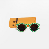 Lunette de soleil pour enfant à monture ronde motif vichy vert et rose et son cordon, posée devant leur étui de rangement en feutrine orange marqué "Hop'Pop".