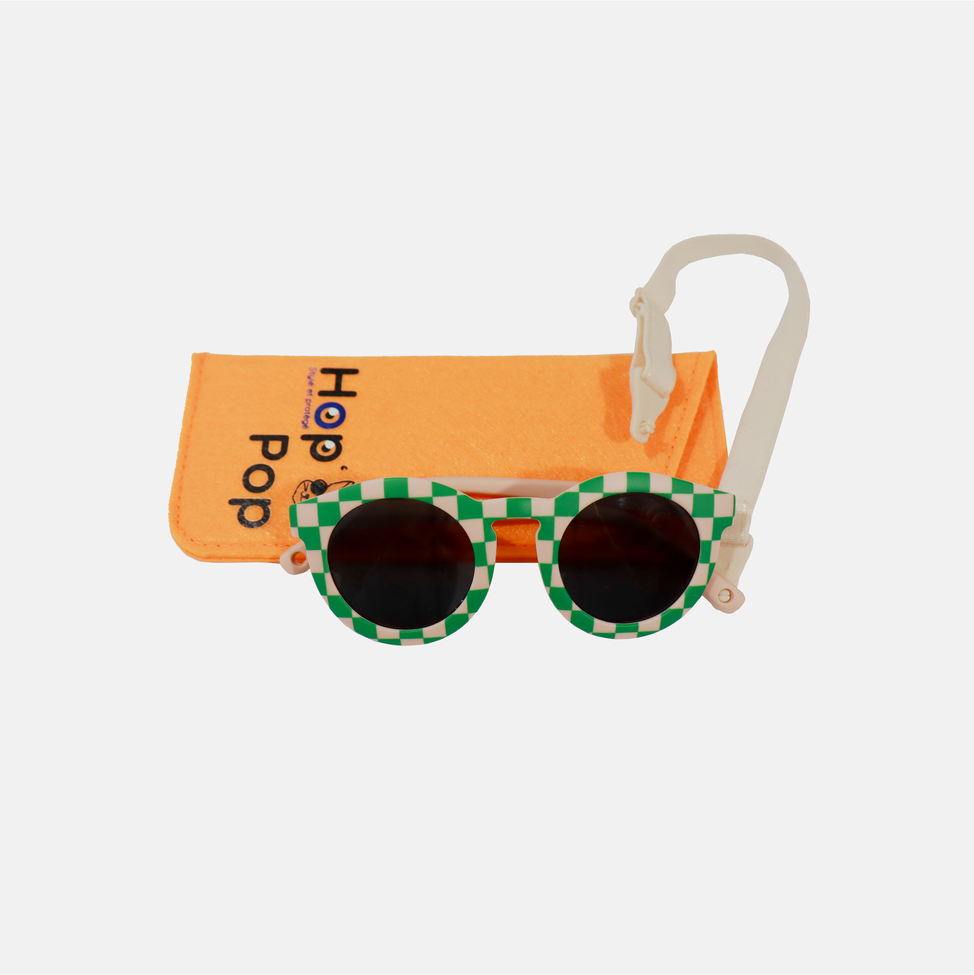 Lunette de soleil pour enfant à monture ronde motif vichy vert et rose et son cordon, posée devant leur étui de rangement en feutrine orange marqué "Hop'Pop".
