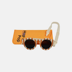 Lunette de soleil pour enfant à monture ronde motif rayée rouge et son cordon, posée devant leur étui de rangement en feutrine orange marqué "Hop'Pop".