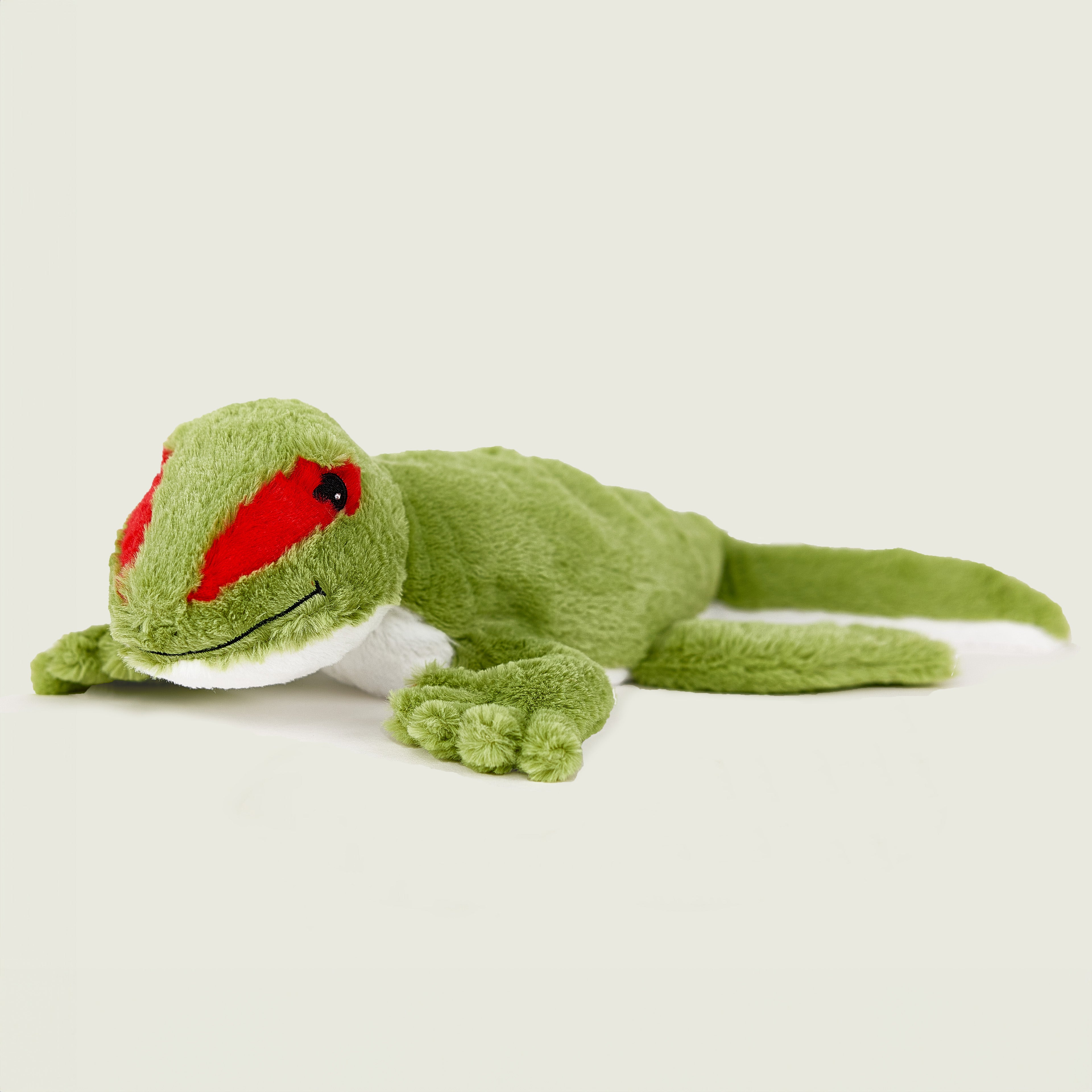 Peluche bouillotte déhoussable gecko verte, corps inférieur blanc, avec visage souriant et aplats rouge au niveau des yeux. Vue de profil