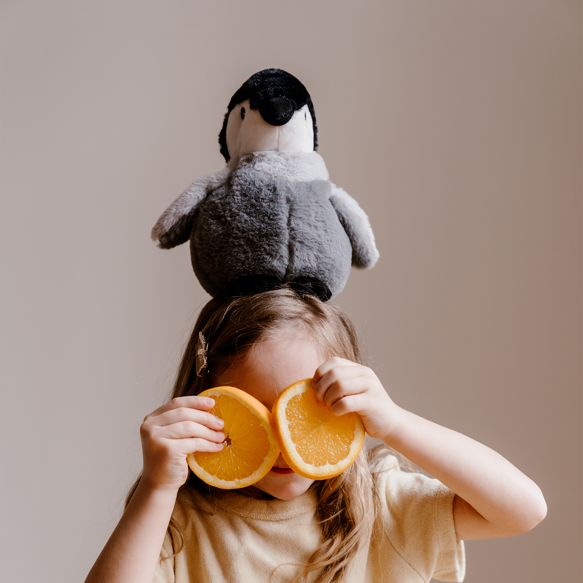 Pingouin bouillotte peluche en situation perché sur la tête d'une fillette 
