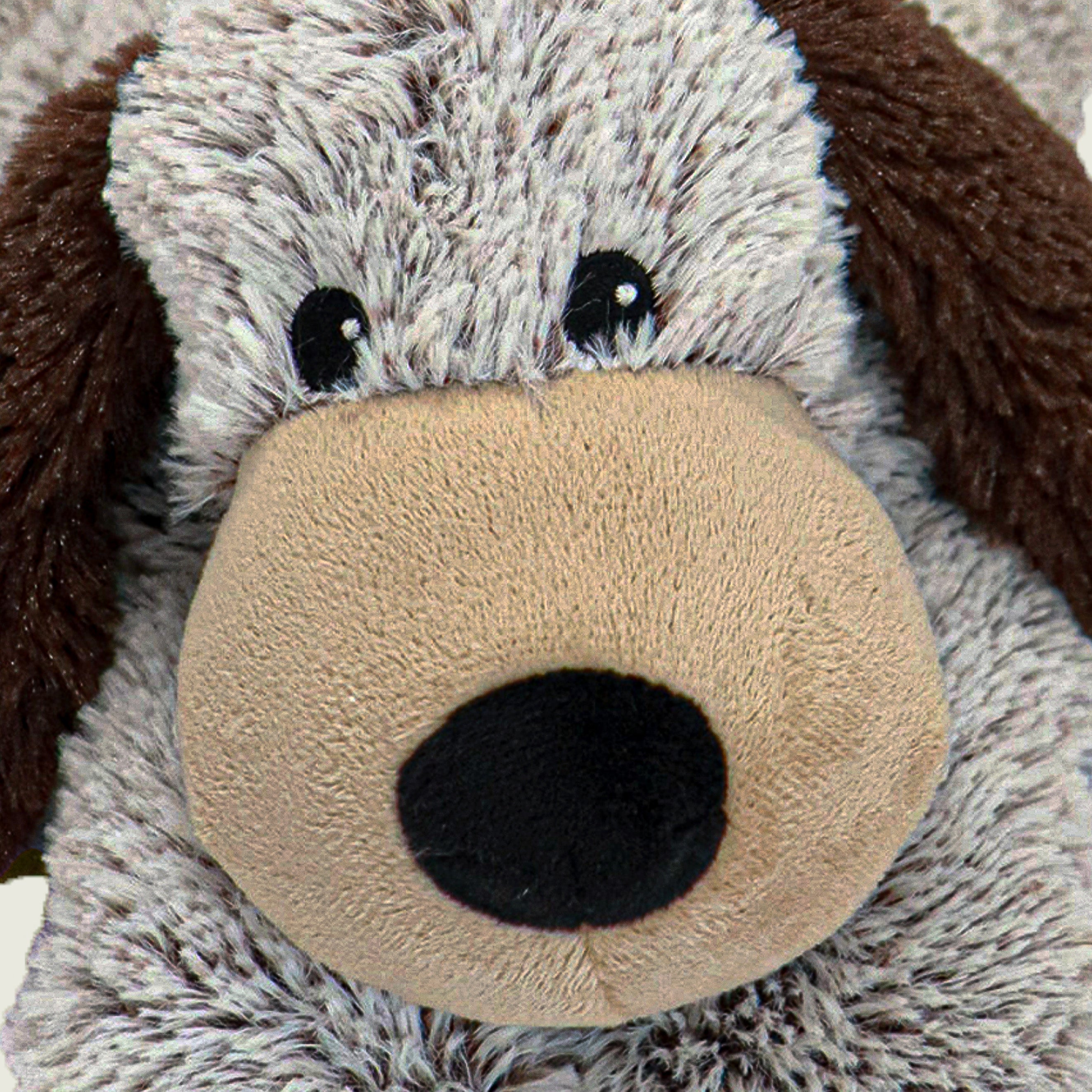 Zoom sur la tête de la bouillotte peluche en forme de chien. Poils gris et marron et museau beige